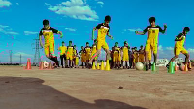 فێرگەیەکی تۆپی پێی منداڵان لە یاریگەی خۆڵدا راھێنان دەکەن