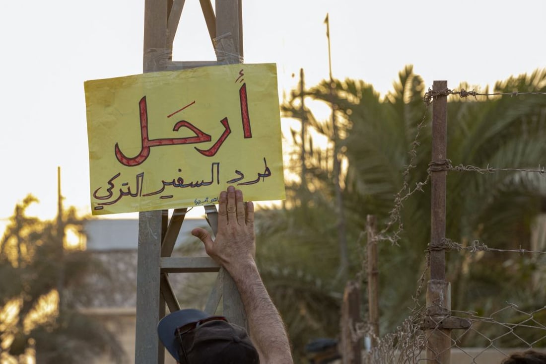 A protester points to a poster calling for the dismissal of the Turkish ambassador during a demonstration condemning the artillery bombardment of a Kurdish hill village, which Iraq blames on neighbouring Turkey, outside the Turkish consulate in the southern Iraqi city of Basra on July 21, 2022. - An angry and grieving Iraq buried nine holidaymakers, including a newlywed, killed in the artillery bombardment of a Kurdish hill village. Baghdad blames neighbouring Turkey and summoned the Turkish ambassador in protest. Ankara denied its troops were responsible and instead accused rebels of the outlawed Kurdistan Workers Party (PKK). Germany, France and Iran condemned the attack. (Photo by Hussein Faleh / AFP) (Photo by HUSSEIN FALEH/AFP via Getty Images)