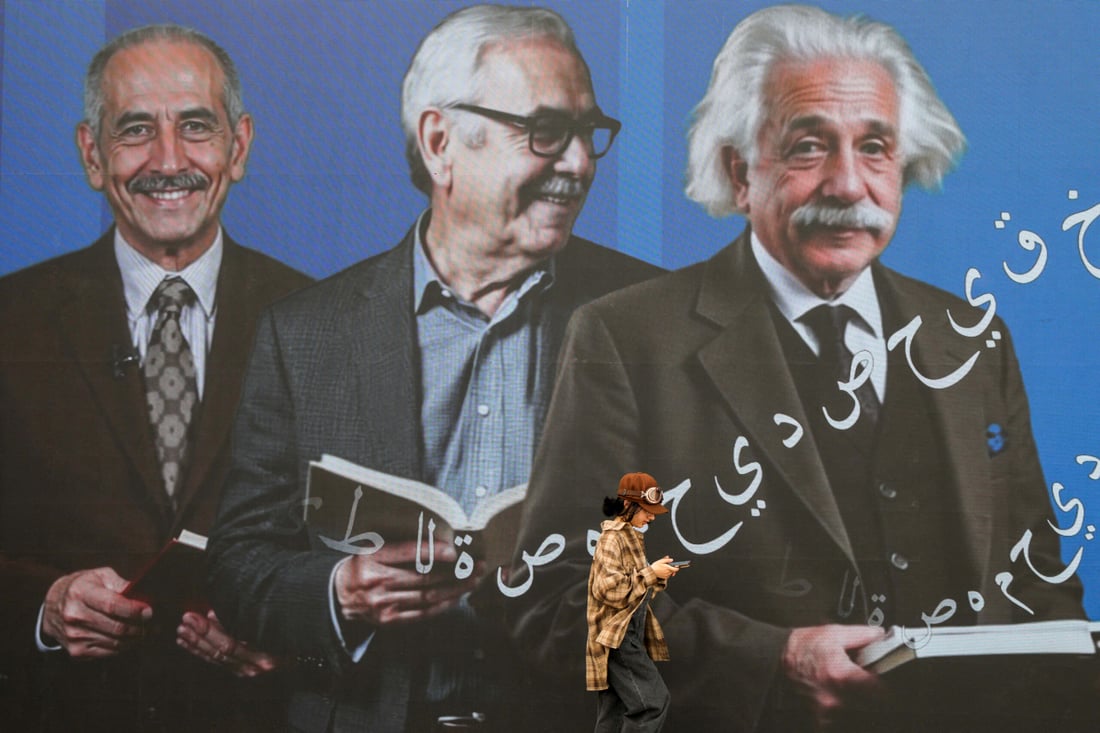 A visitor walks past a large poster during the 17th Arbil International Book Fair, in the capital of the autonomous Kurdish region of northern Iraq, on April 9, 2025. (Photo by Safin HAMID / AFP)