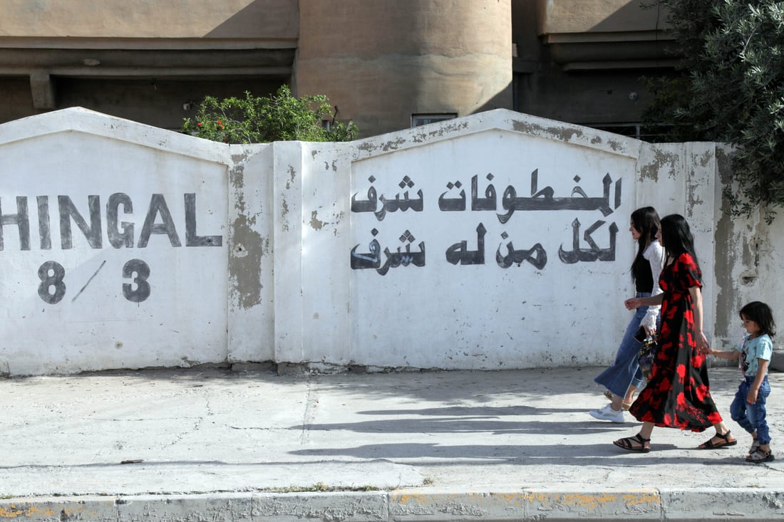 Women accompanied by a child walk along a wall covered in writing in the town of Sinjar. May 6, 2024 (Photo by Safin HAMID / AFP)