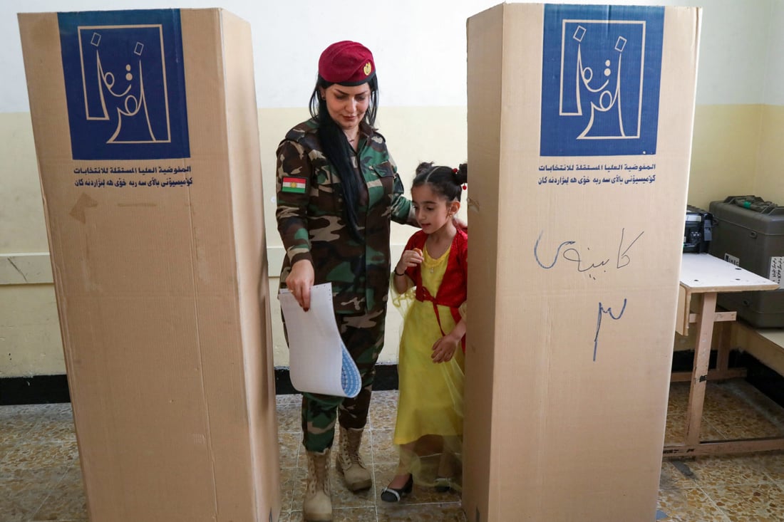 A member of the Kurdish Peshmerga, accompanied by a child, leaves a booth with her ballot (Photo by Safin HAMID / AFP)