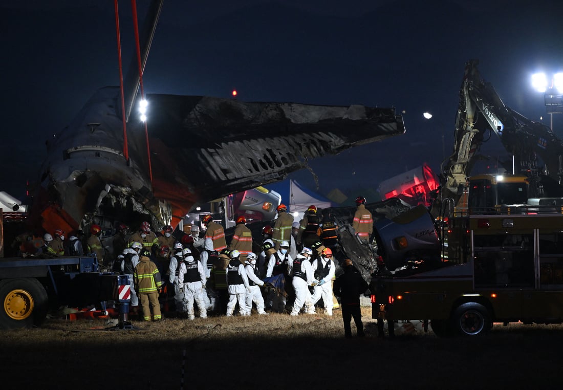 Firefighters and rescue personnel carry the body of a victim near the scene where a Jeju Air Boeing 737-800 series aircraft crashed and burst into flames (Photo by JUNG YEON-JE/AFP)