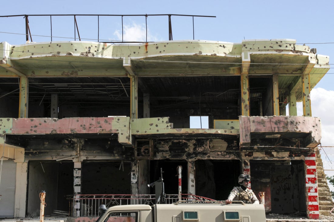 An Iraqi soldier stands in the back of a military vehicle driving past a damaged building. May 6, 2024 (Photo by Safin HAMID / AFP)