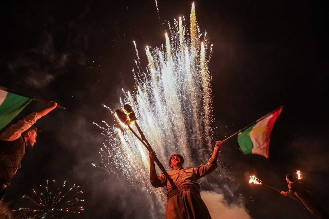 Iraqi Kurds wave flags and hold torches as fireworks light the sky during the Nowruz New Year festival in the town of Akre (Photo by Safin HAMID/AFP)