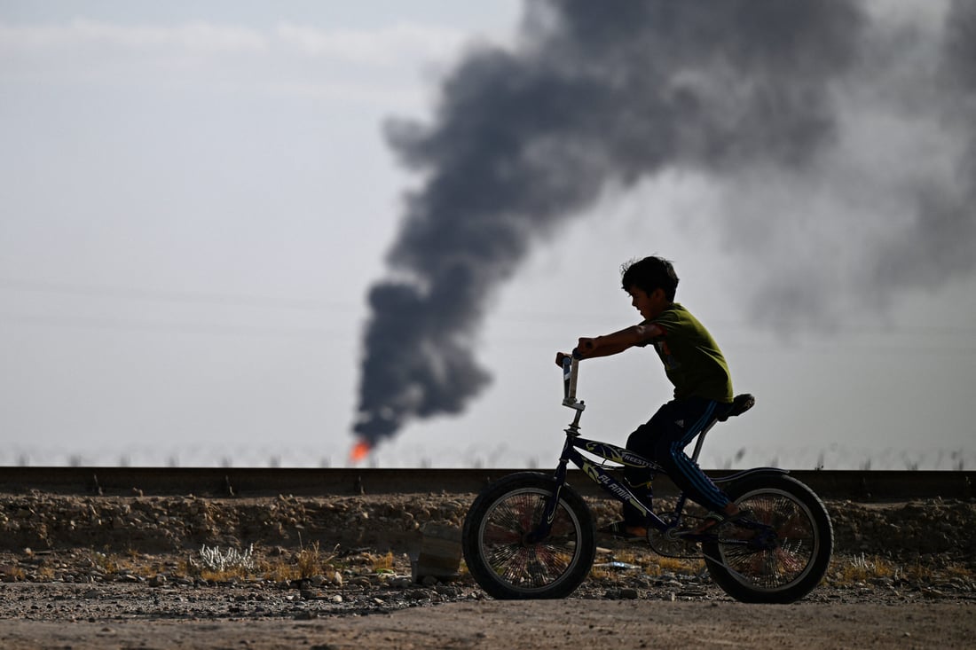 An Iraqi youth rides his bicycle near a flare stack in the Rumaila oil field (Photo by Hussein FALEH / AFP)