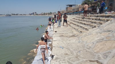 على شط المسيب ومع برودة الفرات.. سباح دولي يدرب الأطفال (صور)