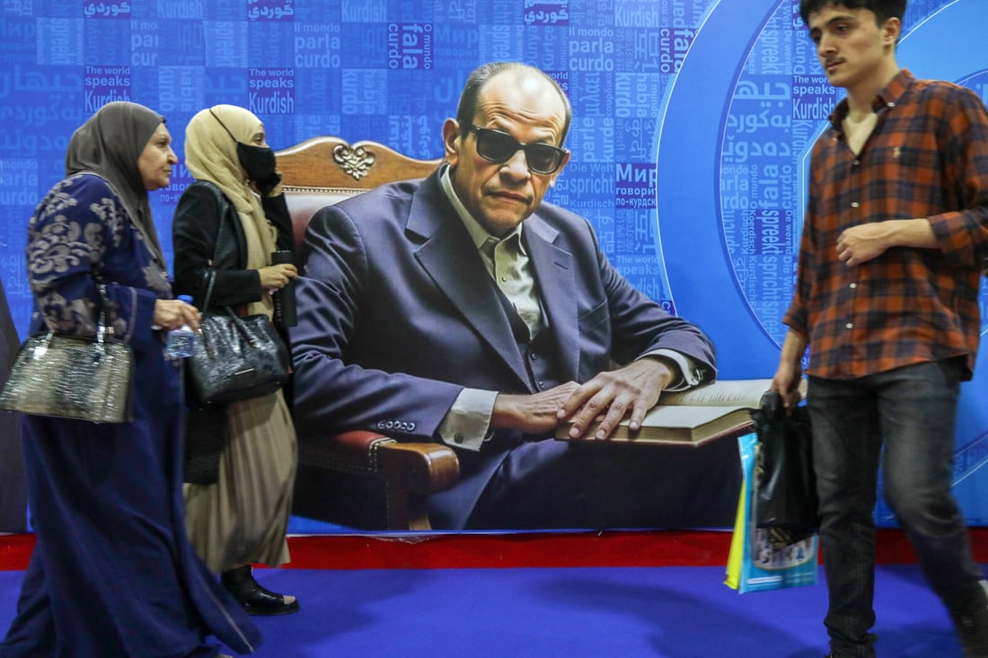 Visitors walk past a poster depicting late Egyptian writer Naguib Mahfouz during the 17th Arbil International Book Fair, in the capital of the autonomous Kurdish region of northern Iraq, on April 9, 2025. (Photo by Safin HAMID / AFP)