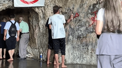 گەشتیارێک بە بۆیاخ دیواری ناوچەیەکى گەشتیارى دەشێوێنێت